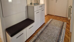A modern, minimalist room with a large white cabinet, a bench, a small table with decorative items, and a patterned rug on a wooden floor.