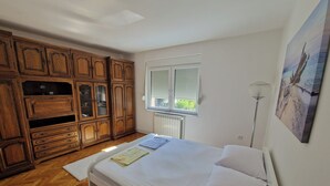 A bedroom with a bed, wooden wardrobe, radiator, window with blinds, and a floor lamp.