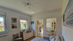 A spacious living area with a grey sofa, a small blue table, and a kitchen in the background.