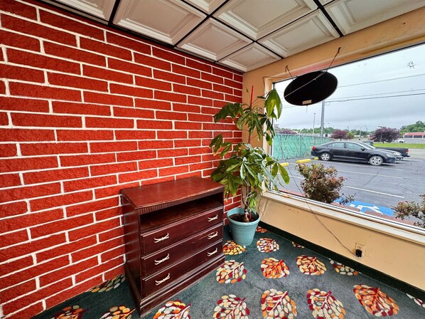 A room with a red brick wall, a wooden cabinet, a potted plant, and a window with a view of a parking lot.