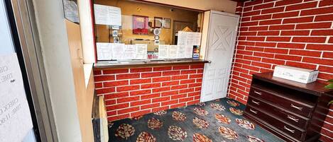 A room with a brick wall, a reception desk with informational posters, a door, and a patterned carpet.