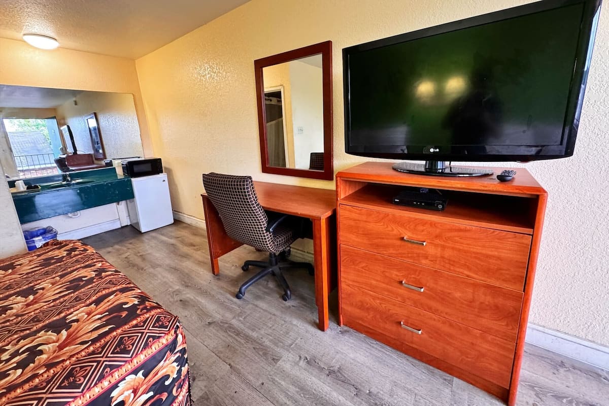 A hotel room with a bed, a desk with a TV, a chair, and a dresser.