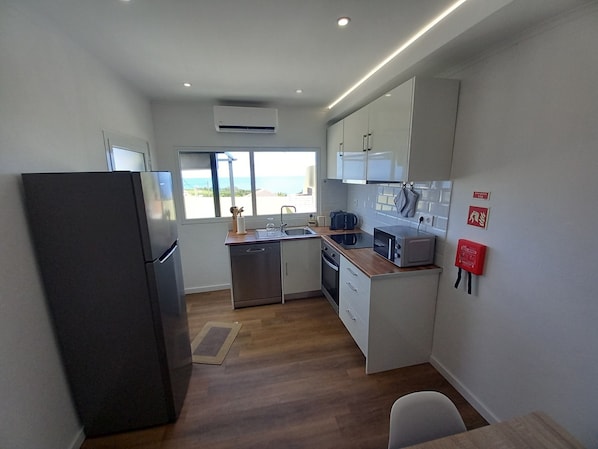 Cocina compacta con refrigerador, pileta y microondas. Una ventana ofrece vistas al exterior.