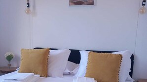 A neatly made bed with white linens and two gold pillows, a framed picture on the wall, and a small vase with flowers on the nightstand. - Charming Rustic House in Nordeste surrounded by nature (Nordeste)