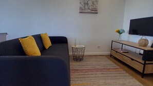 A modern living room with a dark sofa, yellow cushions, a small round table, a TV on a wooden stand, and a painting on the wall. - Charming Rustic House in Nordeste surrounded by nature (Nordeste)