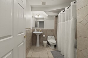A bathroom with a pedestal sink, toilet, and a shower curtain.