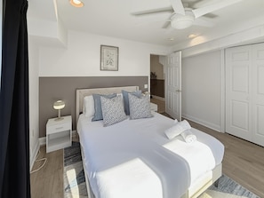 Un dormitorio con cama, mesita de noche, lámpara, ventilador de techo y armario.