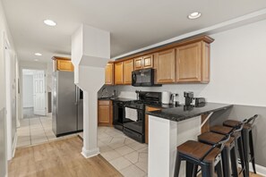 A modern kitchen with wooden cabinets, stainless steel appliances, and a bar area with stools.