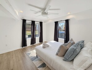 A bedroom with a bed, a ceiling fan, and two windows with curtains.