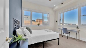A bedroom with a bed, desk, chair, and large windows with a city view. - Charming 2BD by Independence Hall | Sleeps 6 (Philadelphia)