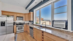 A modern kitchen with stainless steel appliances, wooden cabinets, granite countertops, and a large window offering a city view. - Charming 2BD by Independence Hall | Sleeps 6 (Philadelphia)