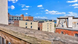 A cityscape with a bridge in the background, various buildings, and a wooden balcony railing. - Charming 2BD by Independence Hall | Sleeps 6 (Philadelphia)