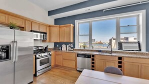 A modern kitchen with wooden cabinets, stainless steel appliances, a dishwasher, and a window with a city view. - Charming 2BD by Independence Hall | Sleeps 6 (Philadelphia)