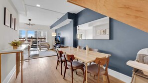 A modern dining area with a large table, chairs, and a city view through large windows.