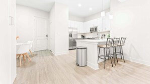 Una cocina moderna con armarios blancos, electrodomésticos de acero inoxidable y una isla central con taburetes.