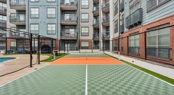 An outdoor tennis court with a net, surrounded by multi-story buildings with balconies and windows.