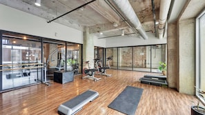 Un gimnasio con equipo de ejercicio, piso de madera y ventanas amplias.