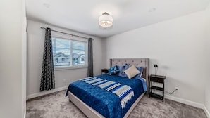 A bedroom with a bed, a nightstand, a lamp, and a window with curtains. - Cozy beautiful house (Calgary)
