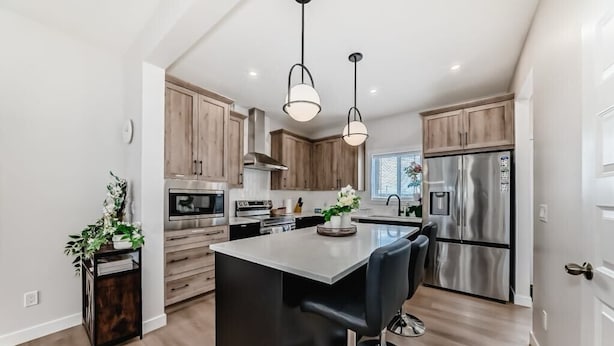A modern kitchen with wooden cabinets, stainless steel appliances, a central island with bar stools, and pendant lighting. - Cozy beautiful house (Calgary)