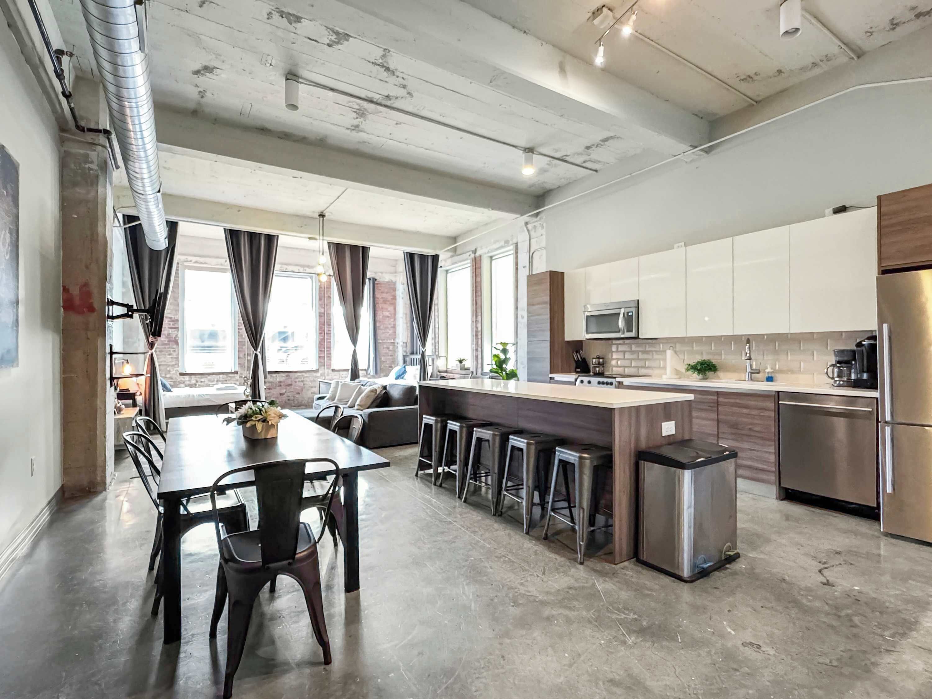 Een moderne keuken met roestvrijstalen apparatuur, een centraal eiland met krukken, en een eethoek met een tafel en stoelen.