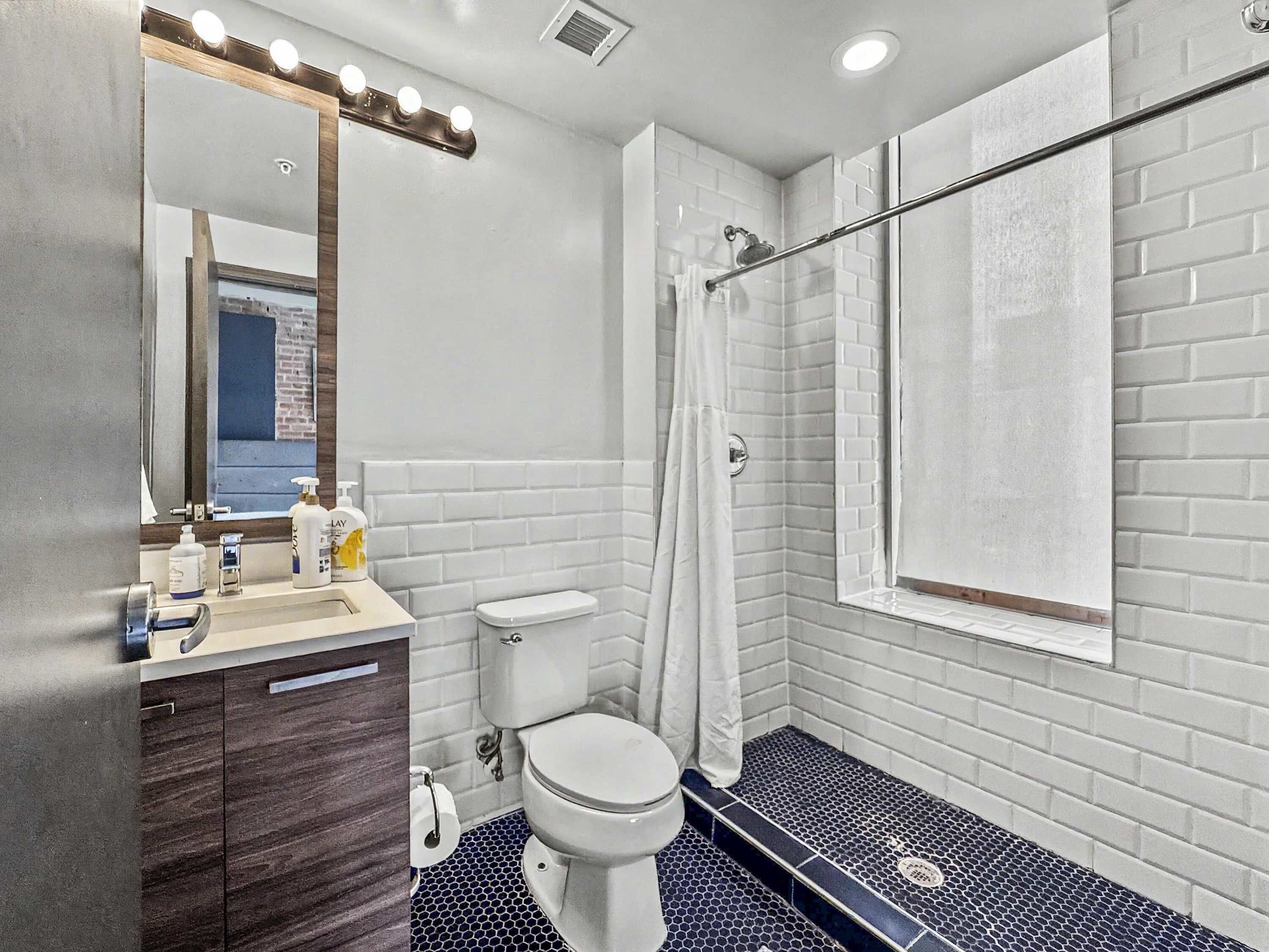 A modern bathroom with a toilet, sink, mirror, and shower area.