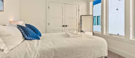 A bedroom with a bed, pillows, a bedside table, a floor lamp, and a window with a view of the outside.