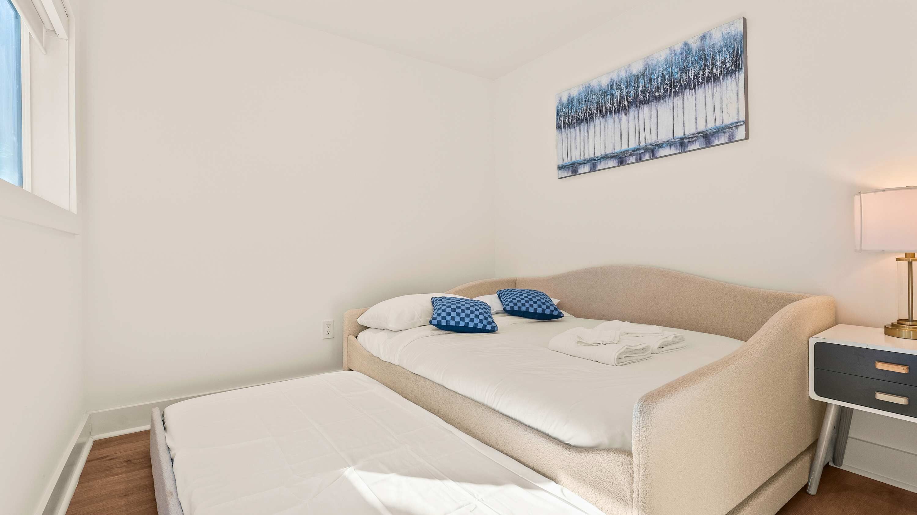 Un dormitorio con una cama, una mesita de noche, una lámpara y un cuadro en la pared.
