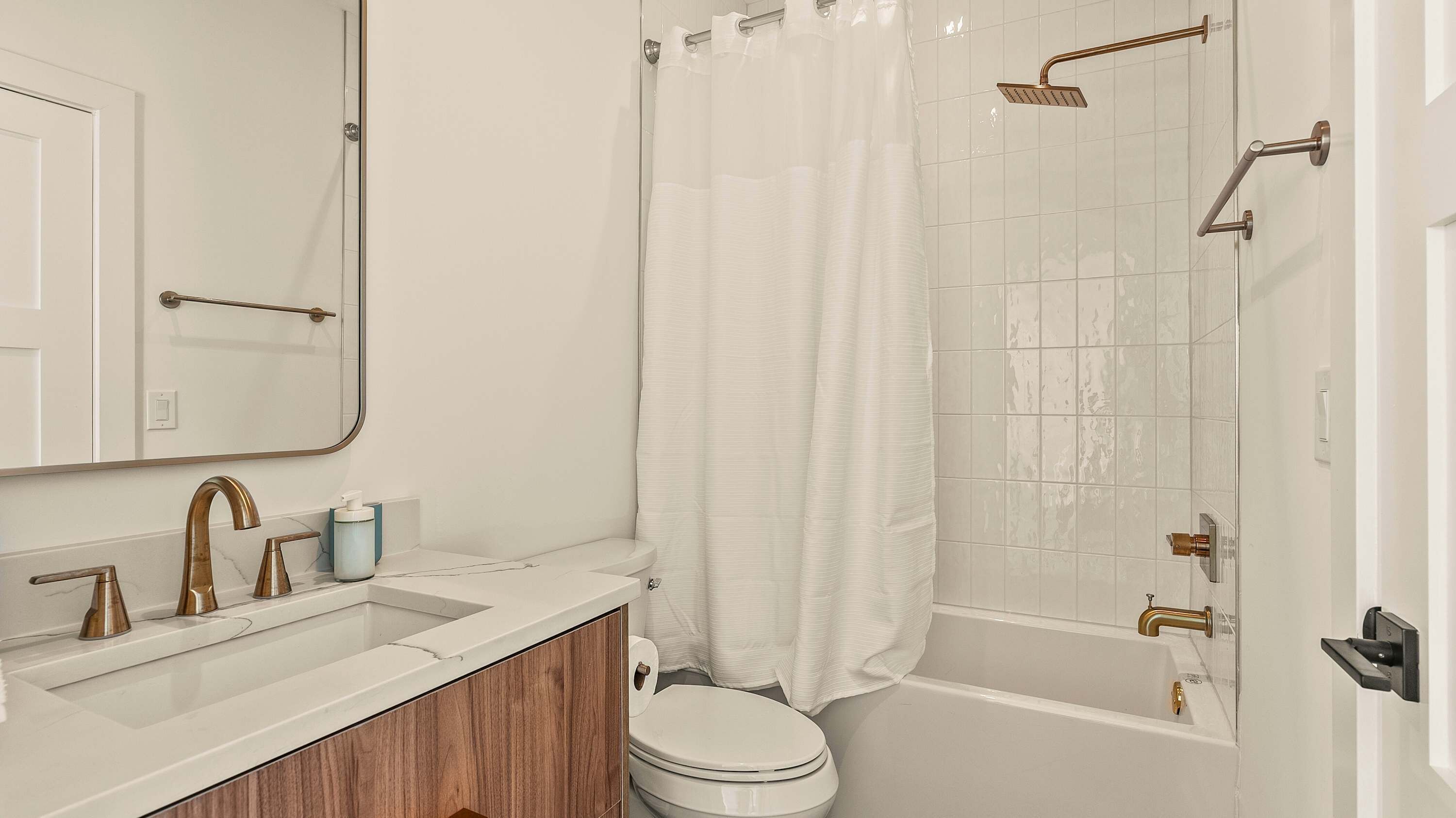 A modern bathroom with a white sink, vanity, and toilet. It includes a shower with a glass door and a handheld showerhead.