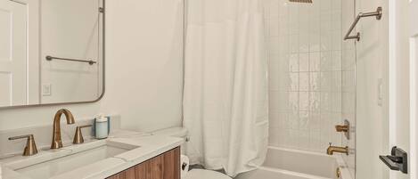 A modern bathroom with a white sink, vanity, and toilet. It includes a shower with a glass door and a handheld showerhead.