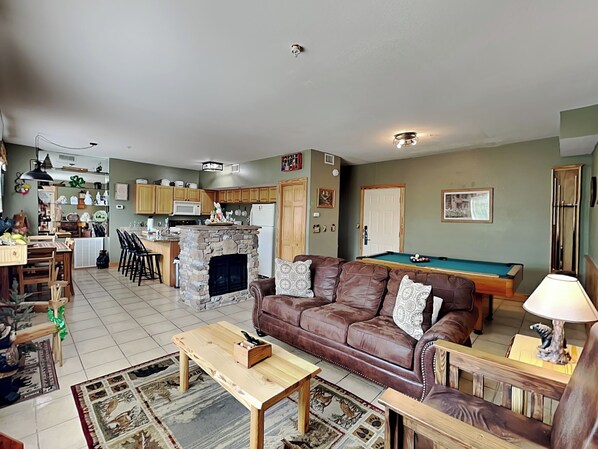 A living room with a fireplace, a pool table, a brown leather sofa, and a dining area with wooden furniture. - Up To Par 3211 by Jackson Mountain Rentals (Pigeon Forge)