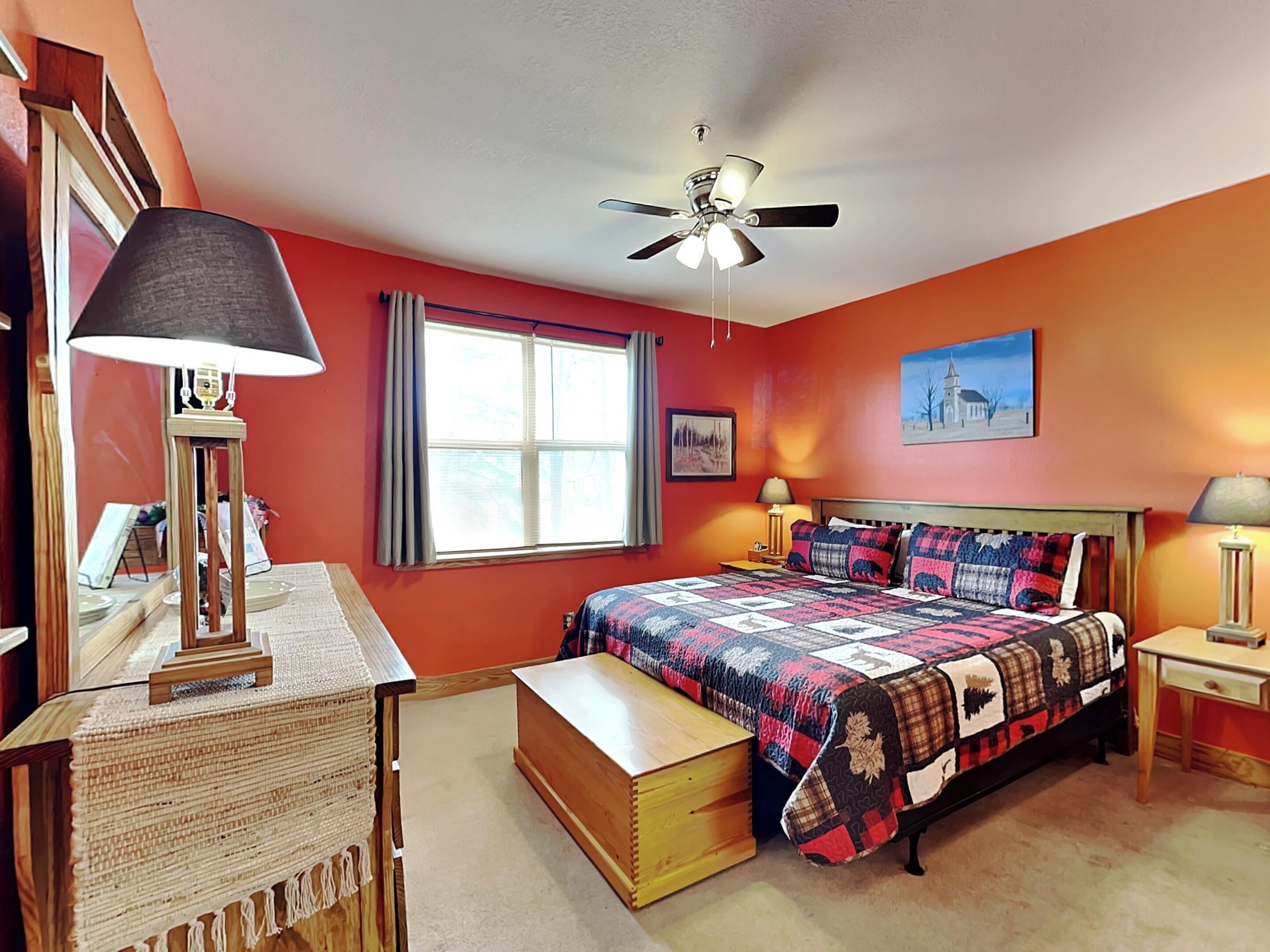 A bedroom with a bed, a desk, a chair, a ceiling fan, and a window with curtains.