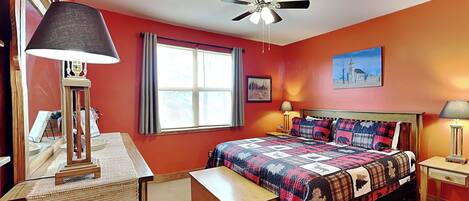 A bedroom with a bed, a desk, a chair, a ceiling fan, and a window with curtains.