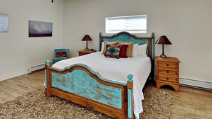 A bedroom with a wooden bed, two bedside tables, a nightstand, a chair, and a window with blinds. - Casa Buena by Kokopelli Property Management (Santa Fe)