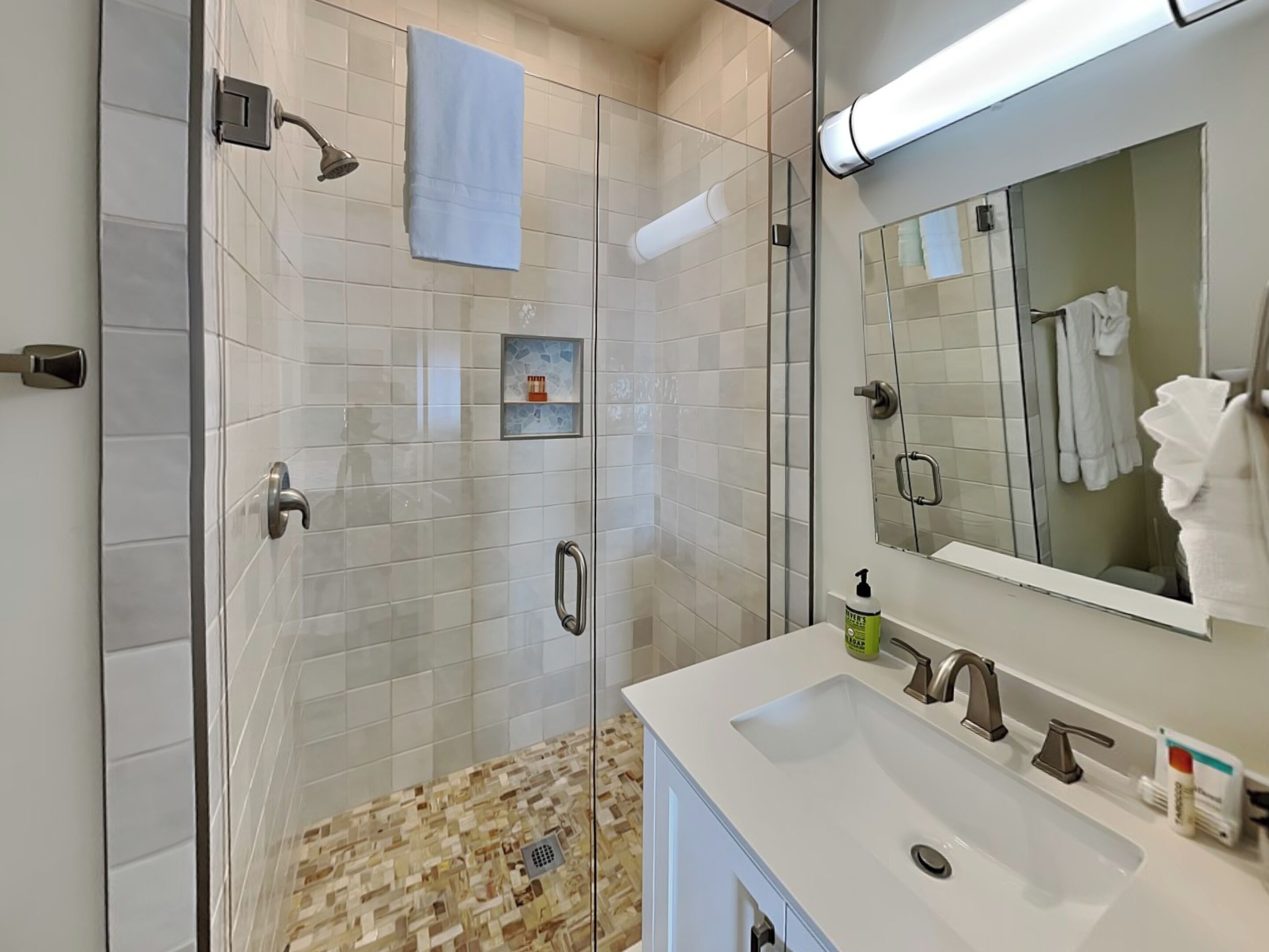 Une salle de bain moderne avec une douche à parois de verre, un lavabo blanc avec un miroir et une petite étagère contenant des articles de toilette.
