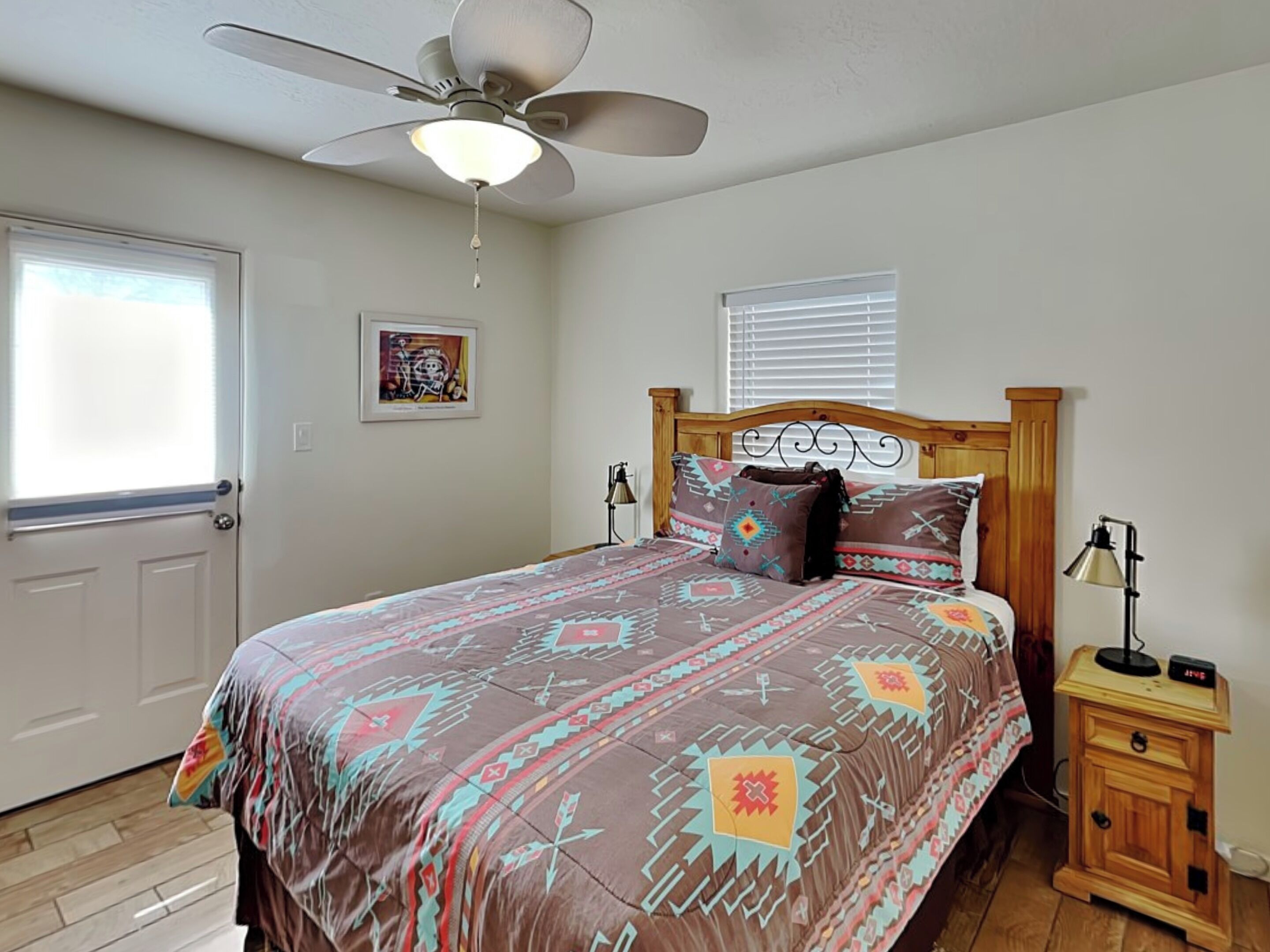 A bedroom with a bed, a ceiling fan, a bedside table with a lamp, and a window with blinds.