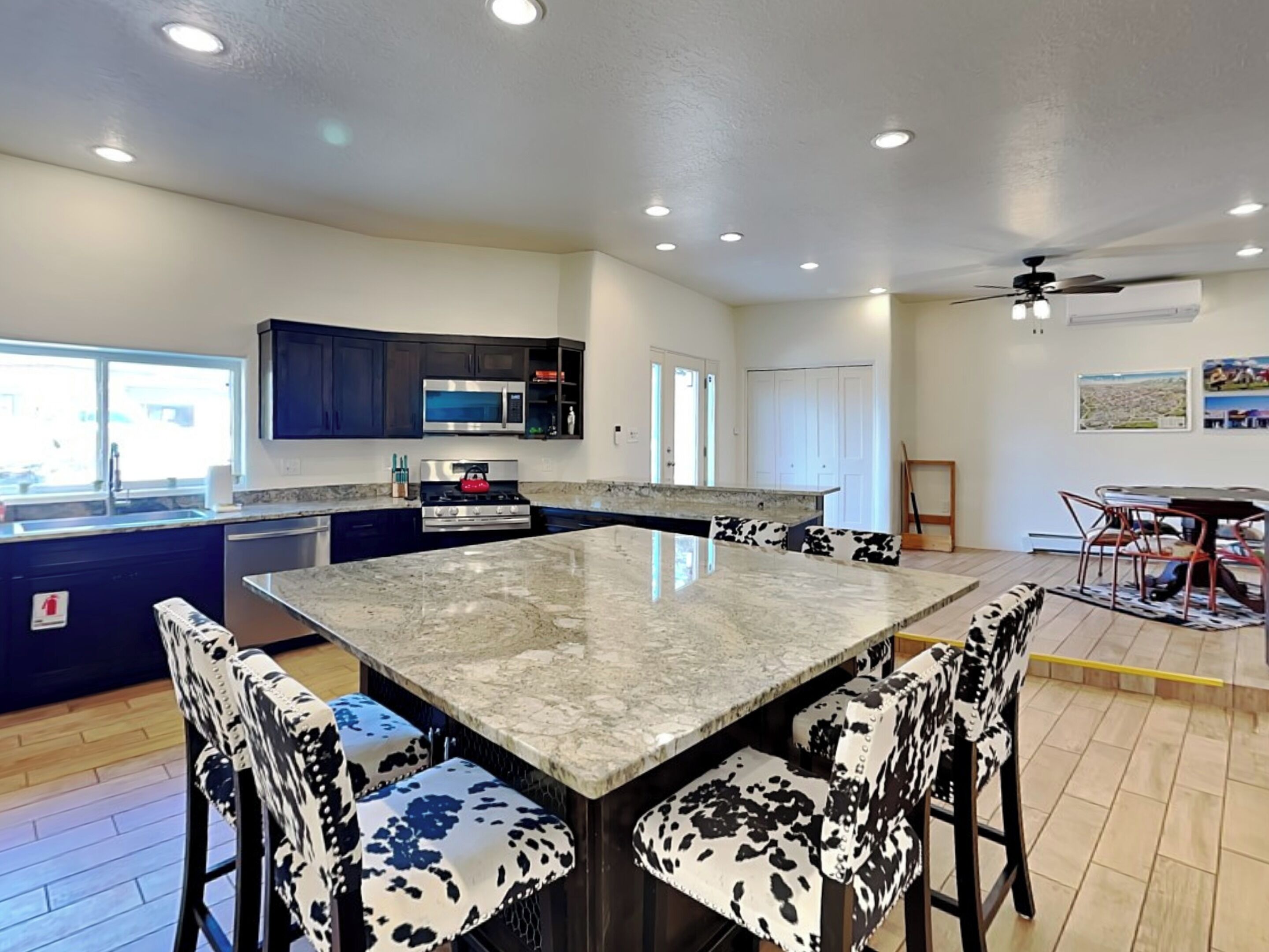 A modern kitchen with a central island, dark blue cabinets, stainless steel appliances, and a dining area with a table and chairs.