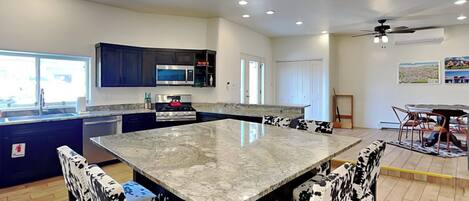 A modern kitchen with a central island, dark blue cabinets, stainless steel appliances, and a dining area with a table and chairs.