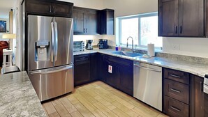 A modern kitchen with dark cabinets, stainless steel appliances, a granite countertop, and a window providing natural light. - Casa Buena by Kokopelli Property Management (Santa Fe)
