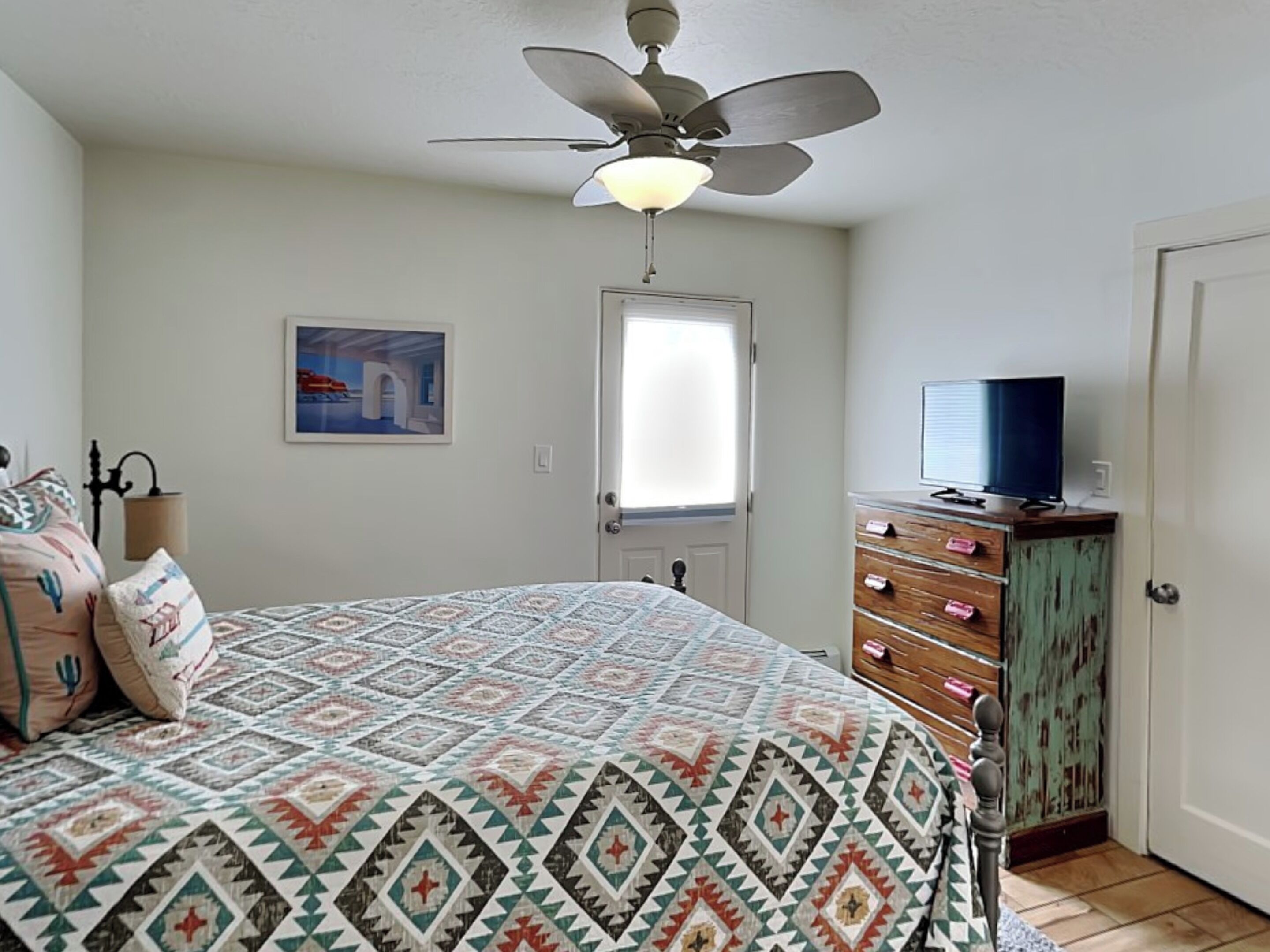 A bedroom with a bed, a ceiling fan, a dresser, and a television.