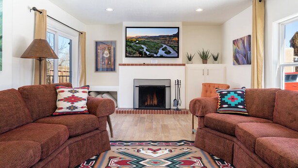 A living room with two brown sofas, a fireplace, a television, and a large window. - Casa Buena by Kokopelli Property Management (Santa Fe)