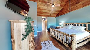Une chambre à coucher au style rustique, avec un lit en bois, un téléviseur fixé au mur et un ventilateur de plafond.