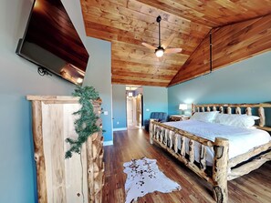 A rustic bedroom with a wooden bed frame, a mounted TV, and a ceiling fan. - 5 Solas Lodge by Jackson Mountain Rentals (Sevierville)