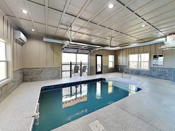 An indoor swimming pool with a view of the outside, a lifeguard station, and a warning sign on the wall.