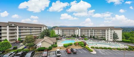 A multi-story hotel with a swimming pool, parking lot, and surrounding greenery.