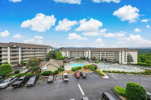 Ein mehrstöckiges Hotel mit Swimmingpool, Parkplatz und umliegender Bepflanzung.