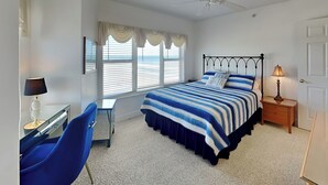 A bedroom with a bed, desk, chair, and a window with blinds.