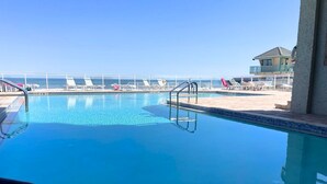 A clear blue pool with a white deck and lounge chairs.