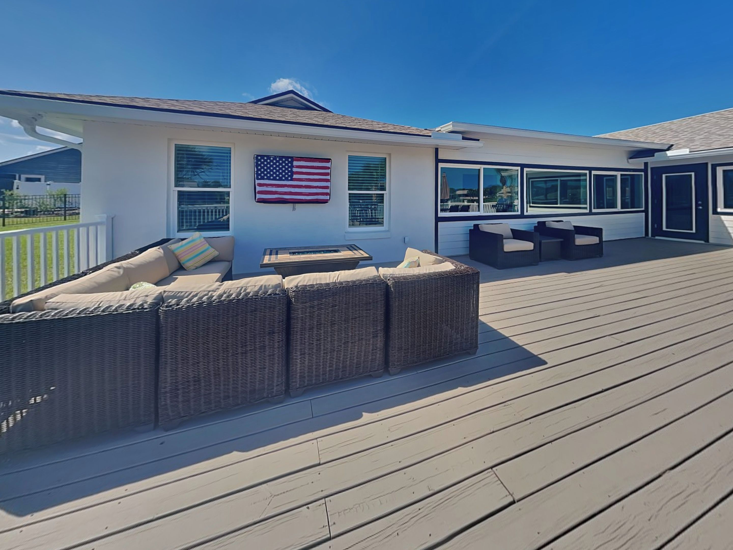 A covered deck with wicker furniture and a large American flag.