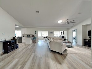 A spacious living area with a large sofa, a dining table, and a kitchen in the background. - Dolphin View Oasis by Distinctive Beach Rentals (Palm Coast)