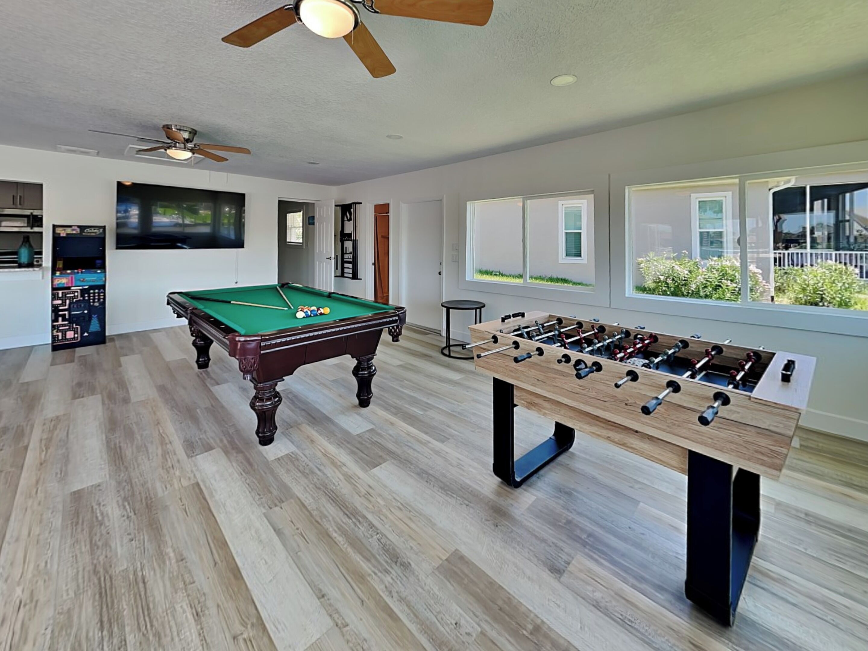 Une pièce spacieuse équipée d’une table de billard, d’un baby-foot et d’un ventilateur de plafond.